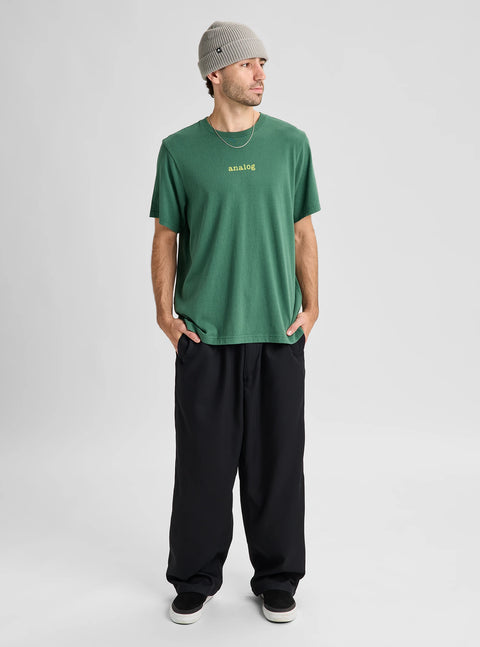 Men's green crew neck t-shirt with yellow Analog logo, worn with black wide-leg pants