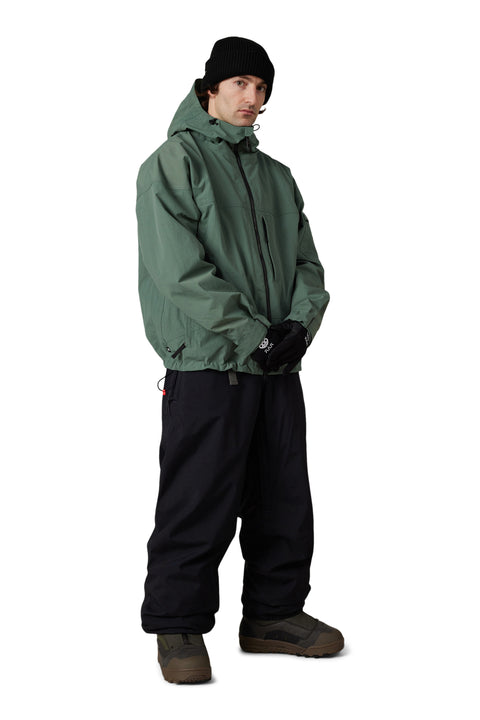 686 Men's Dojo Shell Jacket in sage green with black snow pants and boots
