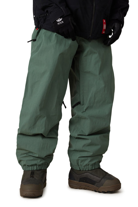 686 Men's Dojo Shell Pant in sage green with elastic cuffs and snowboard boots