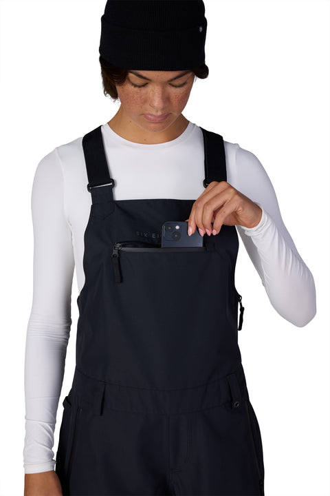 686 Women's Regalia black bib pant with chest zip pocket holding a phone