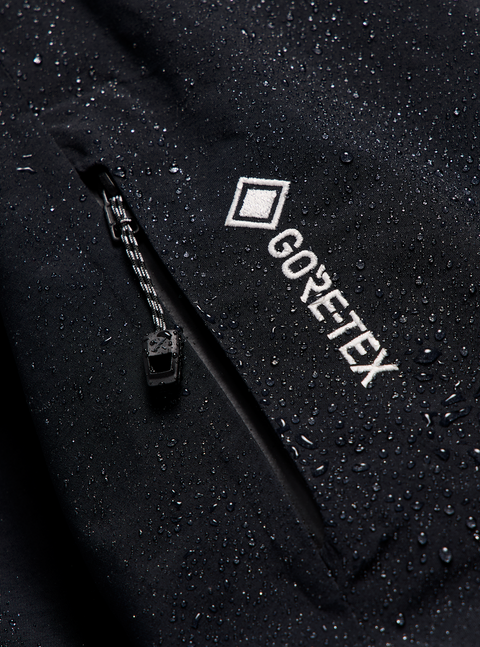 Black GORE-TEX jacket close-up with zipper pocket and embroidered logo, water beading on surface