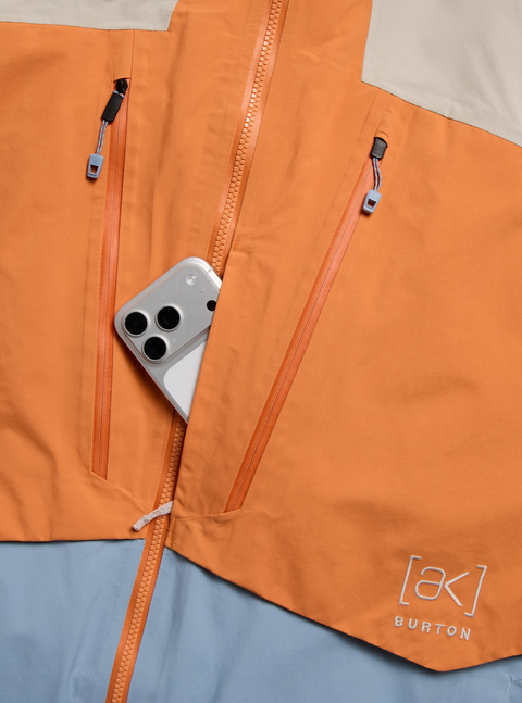 Burton [ak] orange insulated jacket with phone in open chest pocket