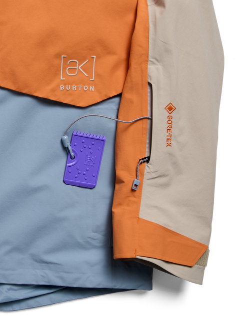 Burton [ak] GORE-TEX jacket in orange, tan, and blue with purple hang tag