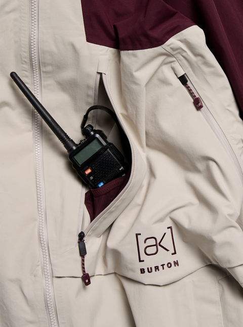 Burton [ak] cream and burgundy jacket pocket holding a walkie-talkie radio