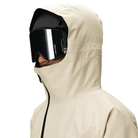 Man wearing a light beige hooded jacket with ski helmet and mirrored goggles, side view