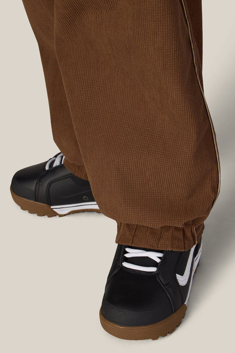 Close-up detail of brown corduroy jogger pant hem with elastic cuff over black sneakers