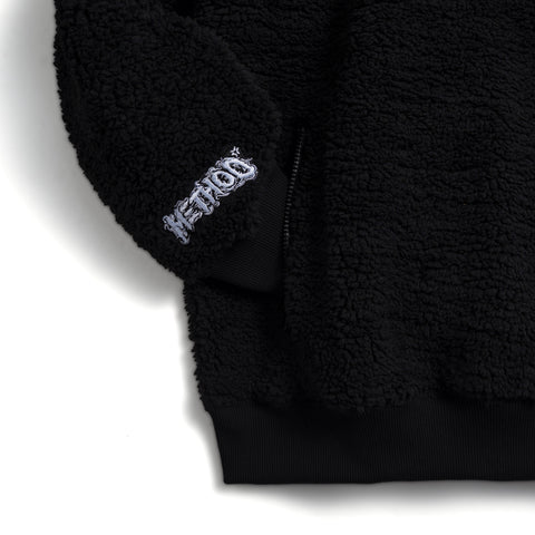 Black sherpa crew sweatshirt detail showing embroidered Method Mag logo patch and zip pocket