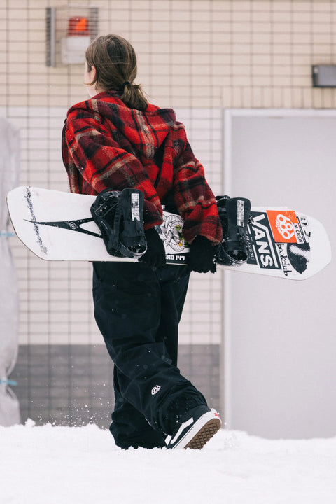 Woman carrying snowboard wearing black 686 Women's Outline Shell Pant in snow