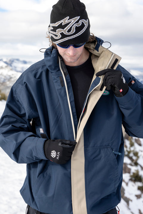 686 men's navy blue ski jacket with tan lining, worn open on snowy mountain