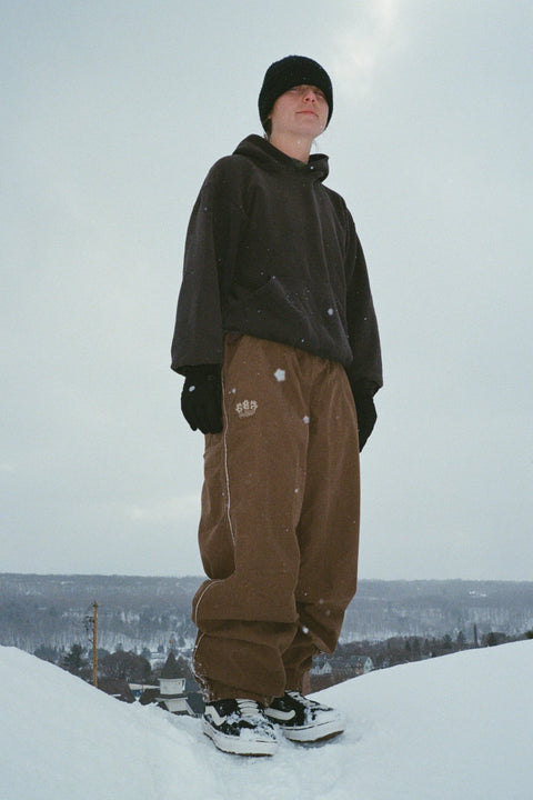 686 Women's Hellkat Shell Pant in brown, worn on snowy hillside with hoodie