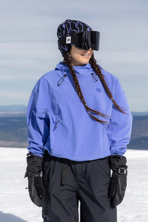 686 Women's periwinkle blue cropped anorak hoodie worn on snowy mountain slope.