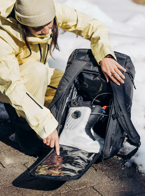 Burton Gig Boot 48L Pack open showing white snowboard boots, worn by woman in yellow jacket
