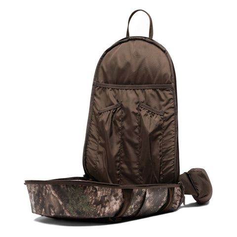 Open sling backpack showing interior organization pockets with camouflage exterior and brown lining