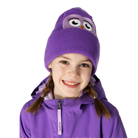 Smiling child wearing a purple owl-faced knit beanie with braided pigtails and matching jacket