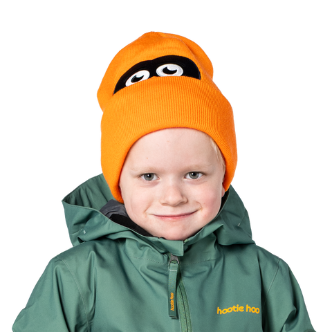 Child wearing bright orange Hootie Hoo beanie with playful owl eyes design and green jacket