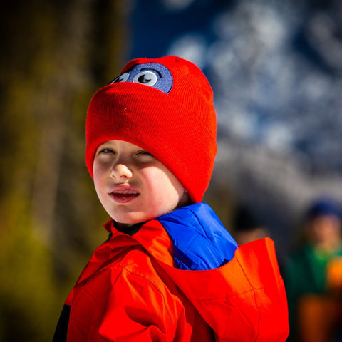 Child wearing red owl-faced beanie with blue accent scarf in outdoor winter setting