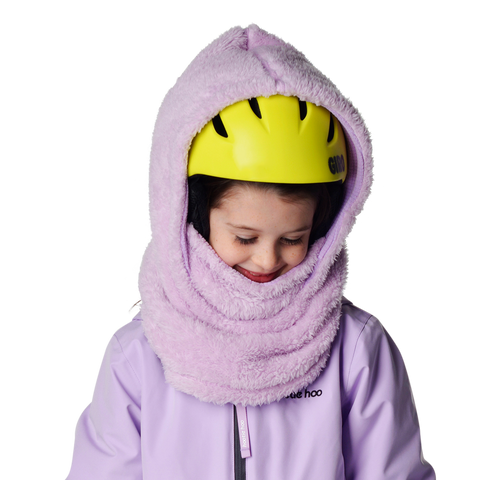 Child wearing a fluffy lavender fleece hood over a yellow ski helmet, smiling downward