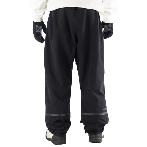 Back view of men's black snow pants with taped seams and snowboard boots