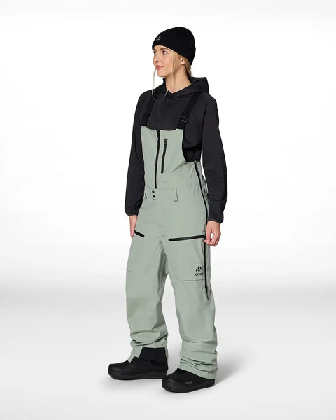 Woman wearing Jones Snowboards bib snow pants with suspenders and black hoodie, front view
