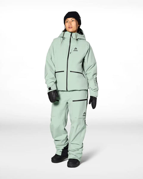 Woman modeling Jones Snowboards insulated jacket and pants in mint green with black gloves and beanie