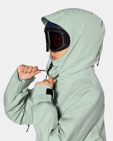 Woman wearing hooded insulated snow jacket with ski goggles, adjusting hood drawcord