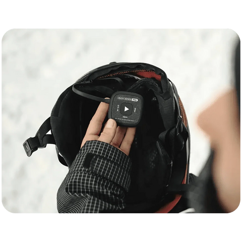 Hand holding black Aleck Snow Series Pro wireless audio module against ski helmet