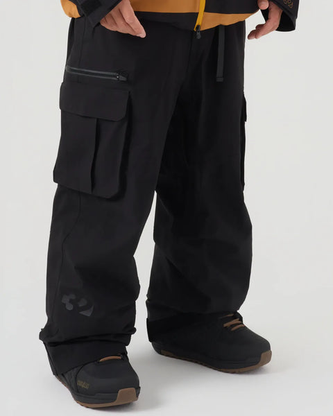 Men's black cargo snow pants with large pockets, worn with snowboard boots, close-up view
